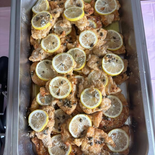 Chicken piccata with lemon slices and capers in a metal serving tray.