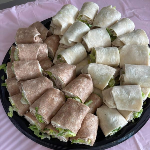 A catering platter filled with an assortment of neatly cut wraps, some whole wheat and some plain.