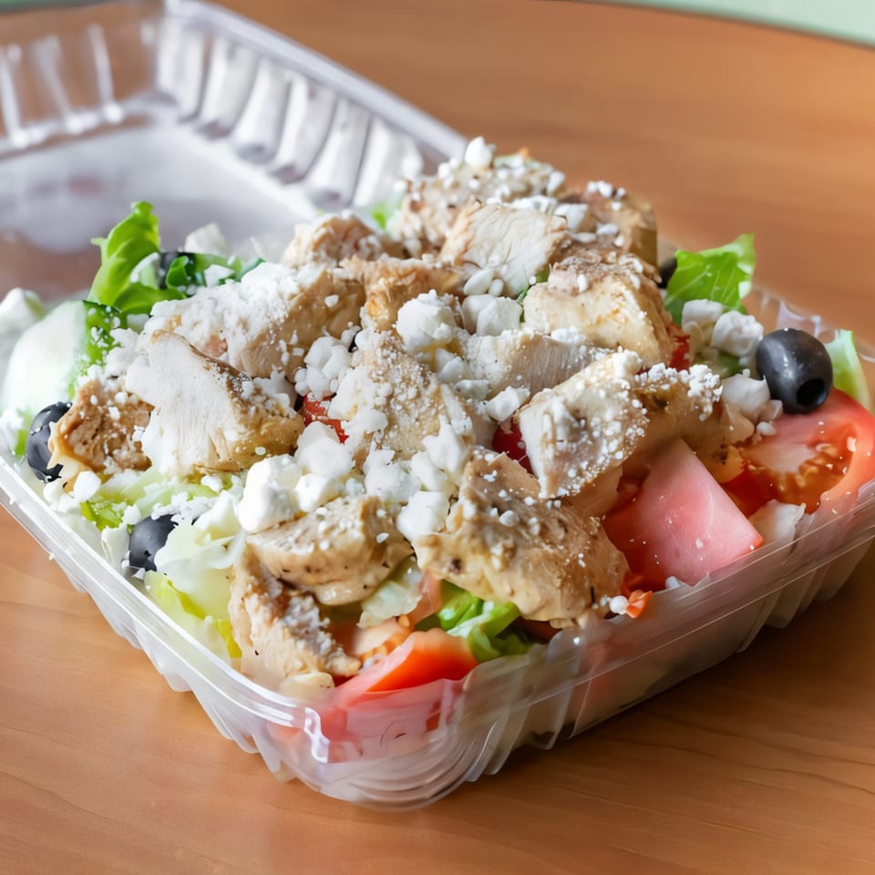 J&M Italian American Cuisine's grilled chicken salad with feta, olives, and tomatoes in a takeout container.
