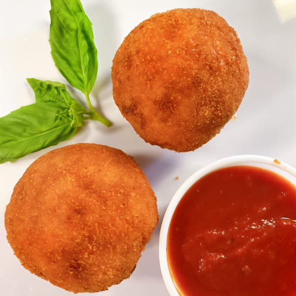 Two golden-fried arancini balls with fresh basil and a side of marinara sauce.