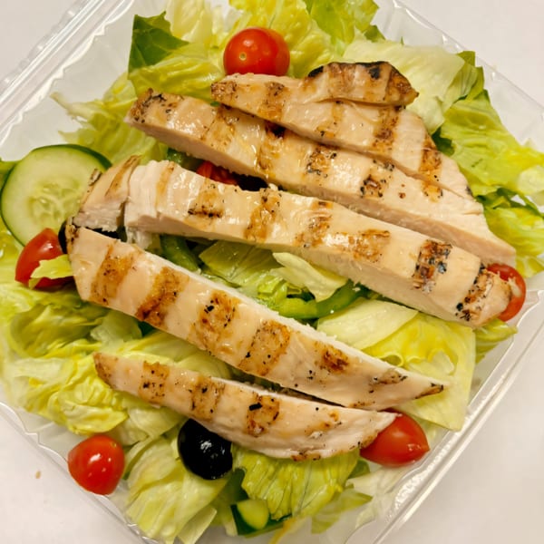 Grilled chicken strips over a fresh salad with lettuce, tomatoes, cucumbers, and olives.