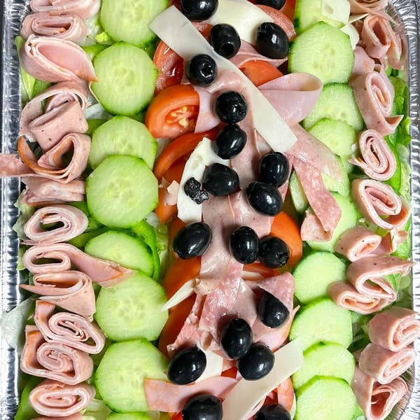 A vibrant Italian salad with rolled meats, cucumbers, tomatoes, cheese, and black olives.