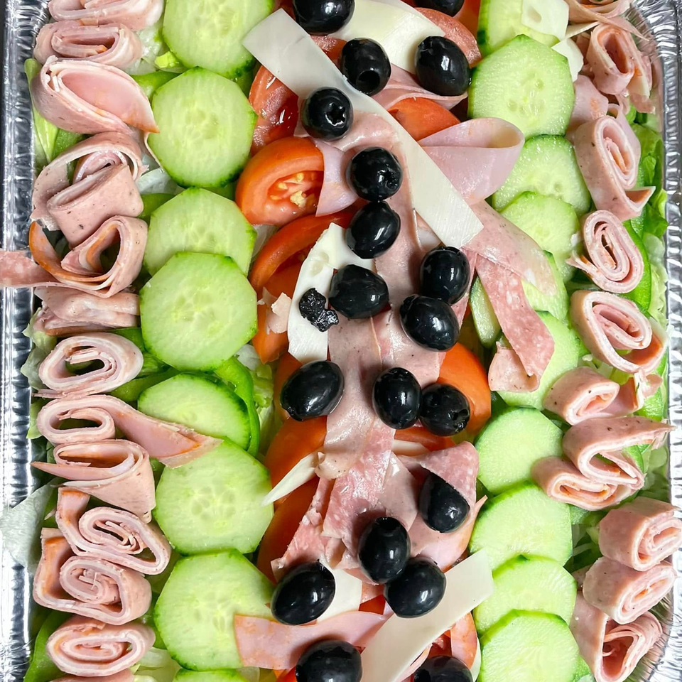 A vibrant Italian salad with rolled meats, cucumbers, tomatoes, cheese, and black olives.